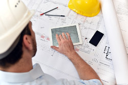 Ein Architekt beugt sich über Baupläne auf einer Baustelle