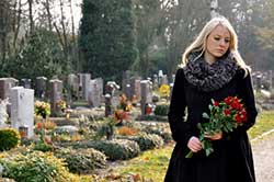 Junge Frau geht mit Blumen über einen Friedhof