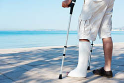 Mann steht mit Gips und Krücken am Strand